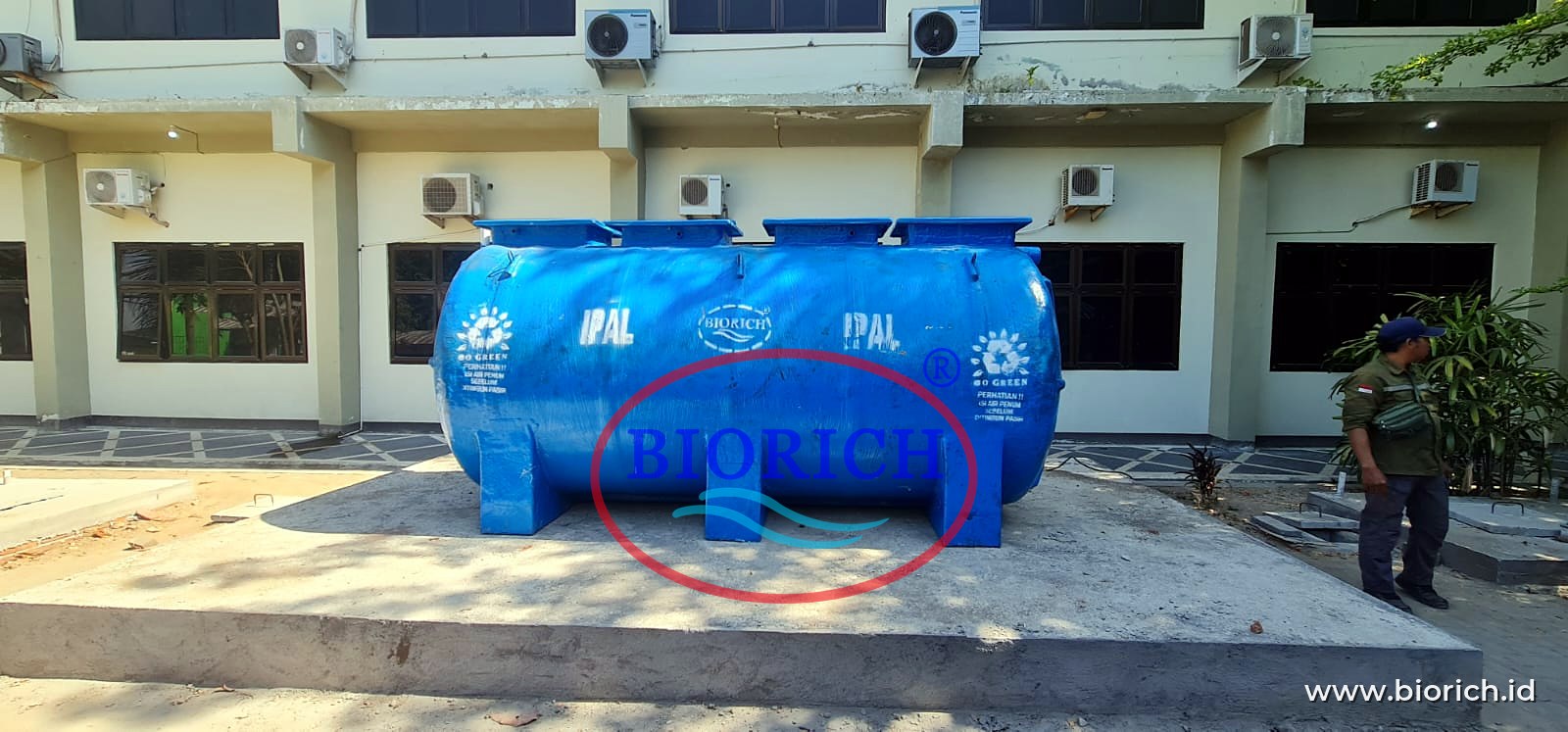 Tangki IPAL BIORICH di atas landasan beton di depan gedung bertingkat sebuah kampus