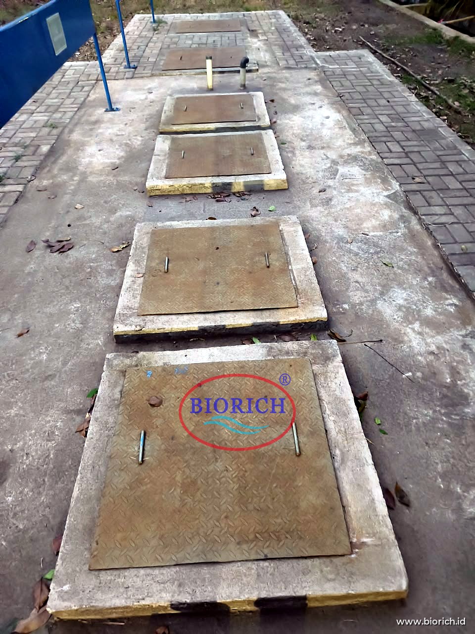 Deretan tutup manhole IPAL yang tertanam di bawah halaman berpaving